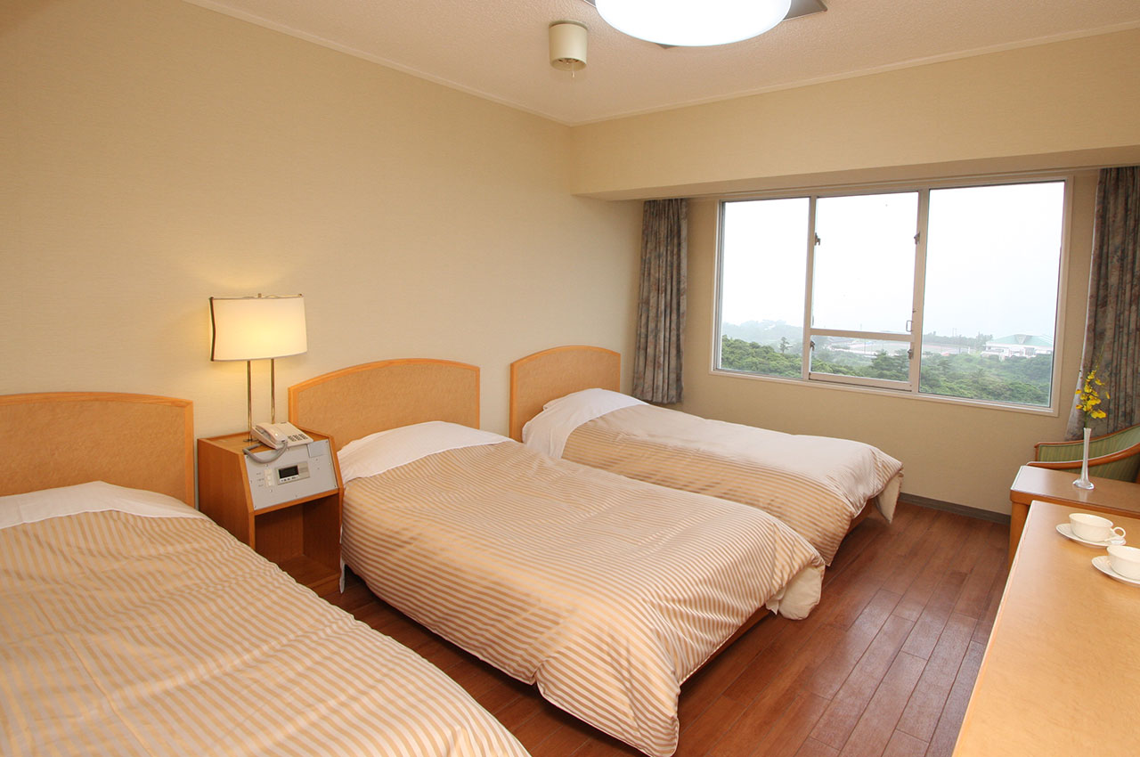ベッドが3つ並ぶ本部グリーンパークホテルのスタンダードルームの写真です。